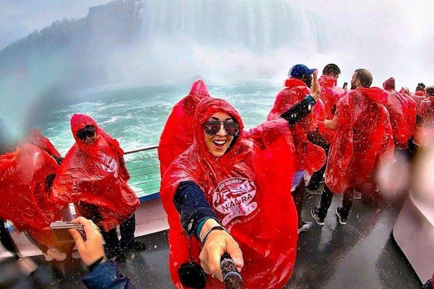 A group of people on a boat wearing red rain ponchos, with a waterfall in the background. 3