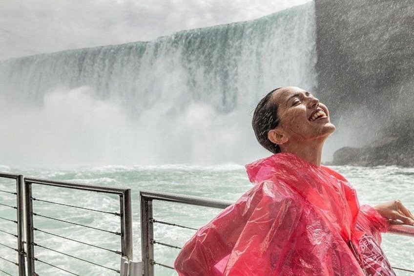 A person in a red raincoat standing by a railing, looking at a waterfall. 4