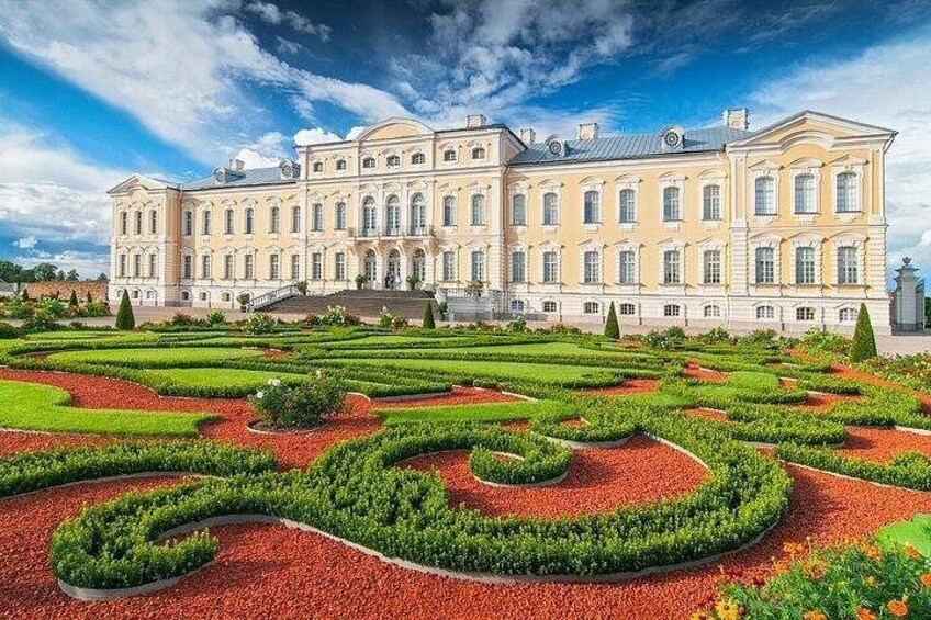 A large classical building with a symmetrical facade, surrounded by a formal garden with geometric patterns and red gravel paths. 5