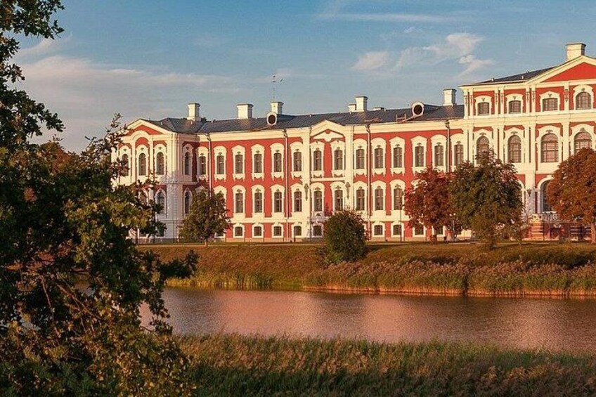 A large, historic building with multiple windows and a symmetrical facade, surrounded by a body of water and greenery. 2