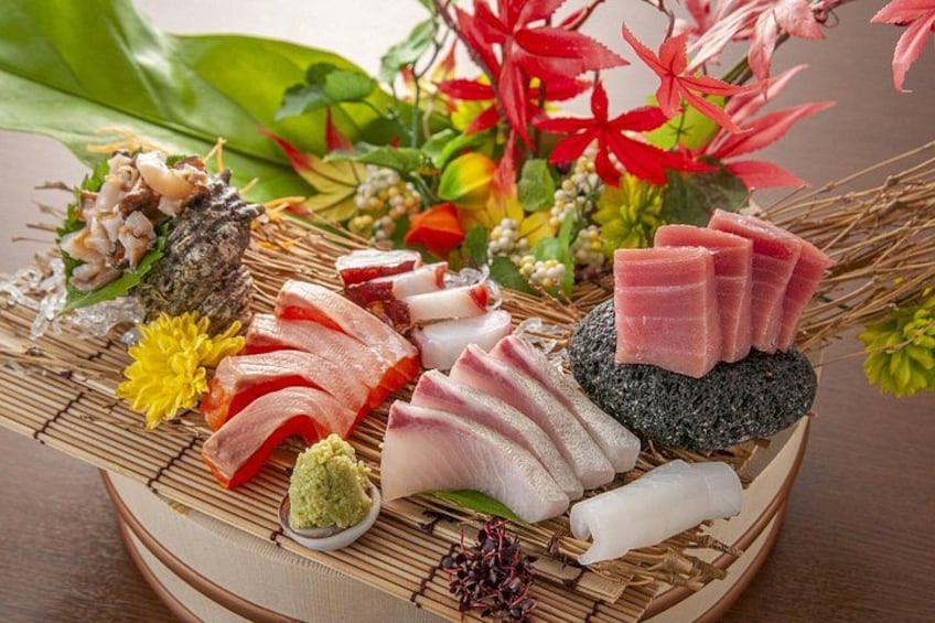 A variety of sushi and sashimi on a bamboo mat, surrounded by decorative flowers and leaves. 1