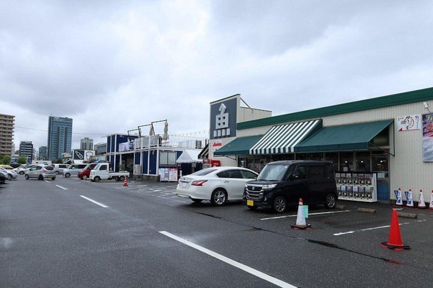 A parking lot with cars, a building with a green awning, and a sign with Japanese characters. 5