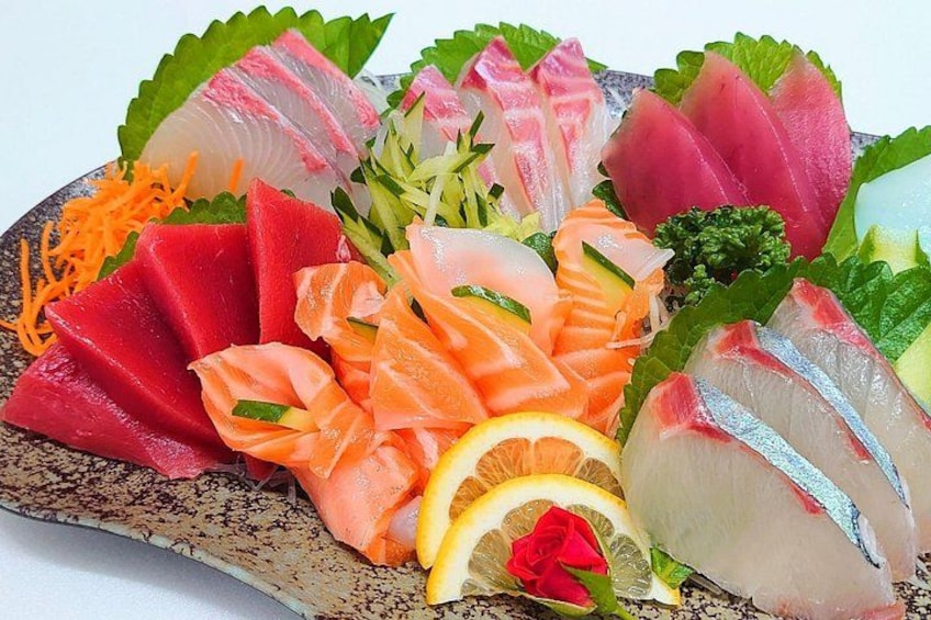 A variety of sashimi on a ceramic plate, including salmon, tuna, and other fish, garnished with vegetables and citrus. 4