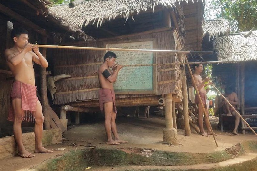 Three individuals outdoors near a thatched-roof structure, possibly engaged in a cultural or traditional activity. 3