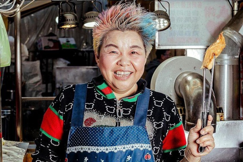 A person holding a large metal ladle, wearing a patterned apron, and standing in a kitchen environment. 5
