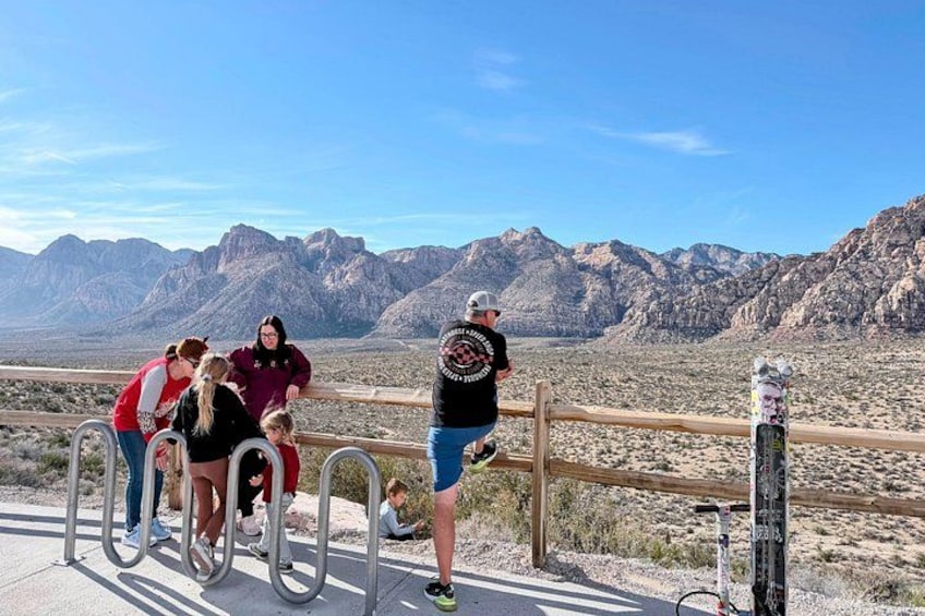 A group of people at a scenic overlook with mountains in the background. 4