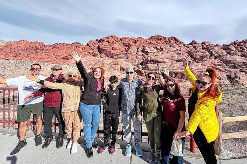 A group of people standing on a wooden platform with a red rock formation in the background. 1