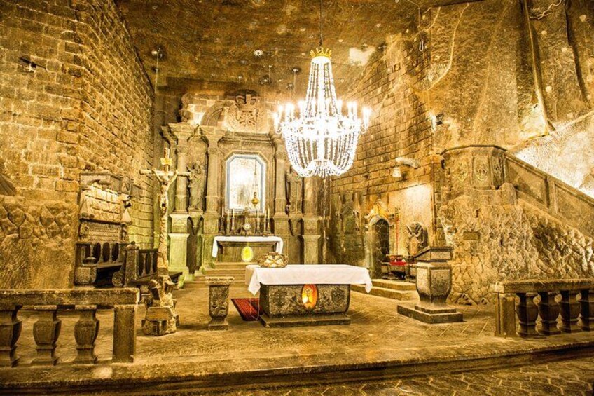 An ancient stone church interior with a chandelier, altar, and stone benches. 5