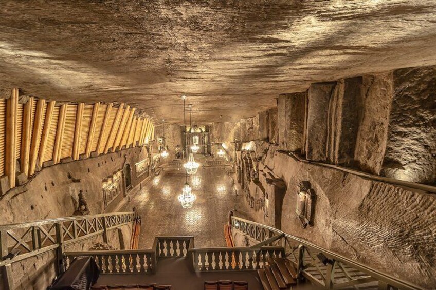 An underground passage with stone walls, chandeliers, and a central staircase. 3