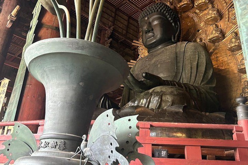 A large Buddha statue, a large metal bowl, and a red railing. 1