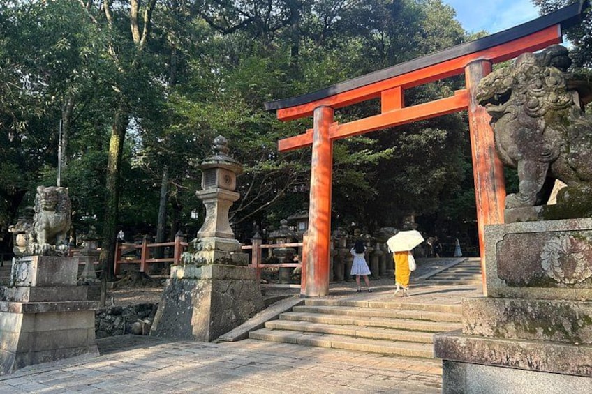 A stone pathway leading to a red torii gate with a stone lion statue on the left. 4