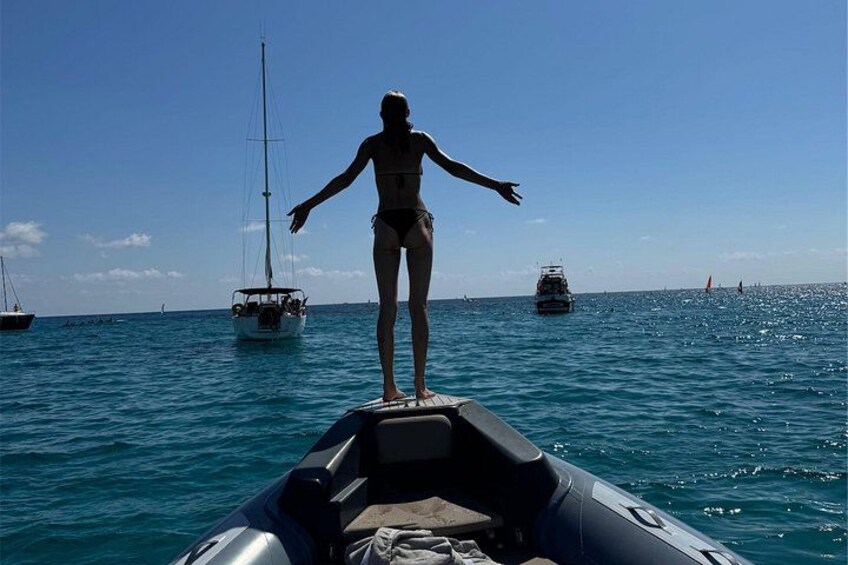 A person standing on a boat with the ocean and sailboats in the background. 4