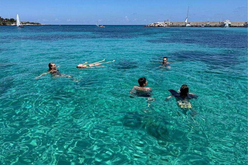 People swimming in clear turquoise water with a distant shoreline and boats. 5