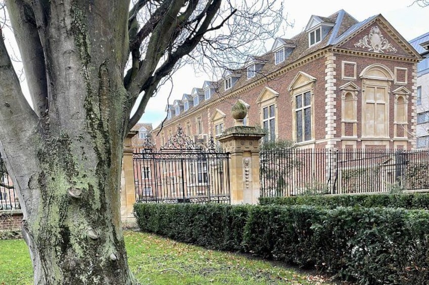 A large brick building with a black iron fence, a tree, and well-maintained hedges. 3