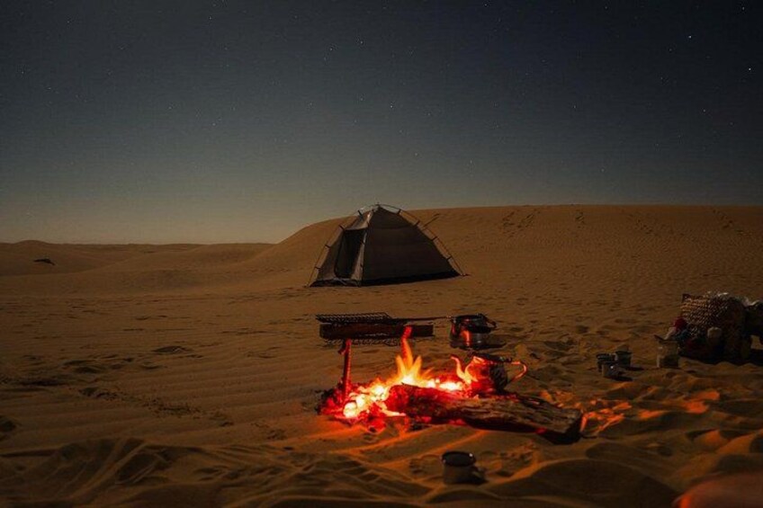 A desert campsite with a tent, a campfire, and a vehicle. 1
