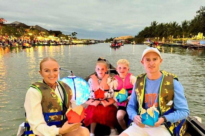 A group of people on a boat, wearing life jackets, with a river and buildings in the background. 5