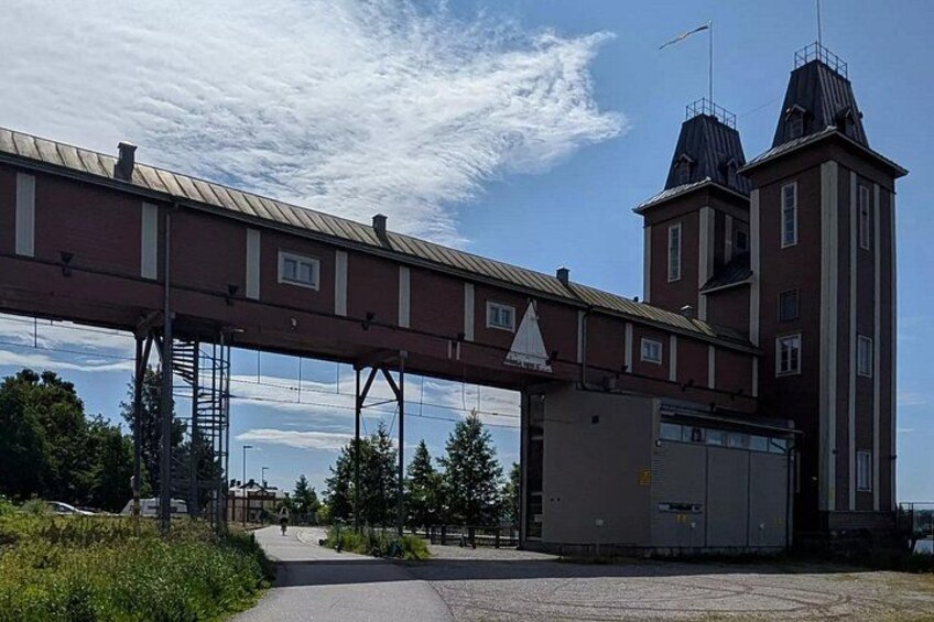 A pedestrian bridge over a road, a building with a red facade, and a tower with a weather vane. 5