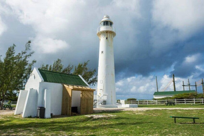 A white lighthouse with a green roof, a small white building with a green roof, and a grassy area with a bench. 1