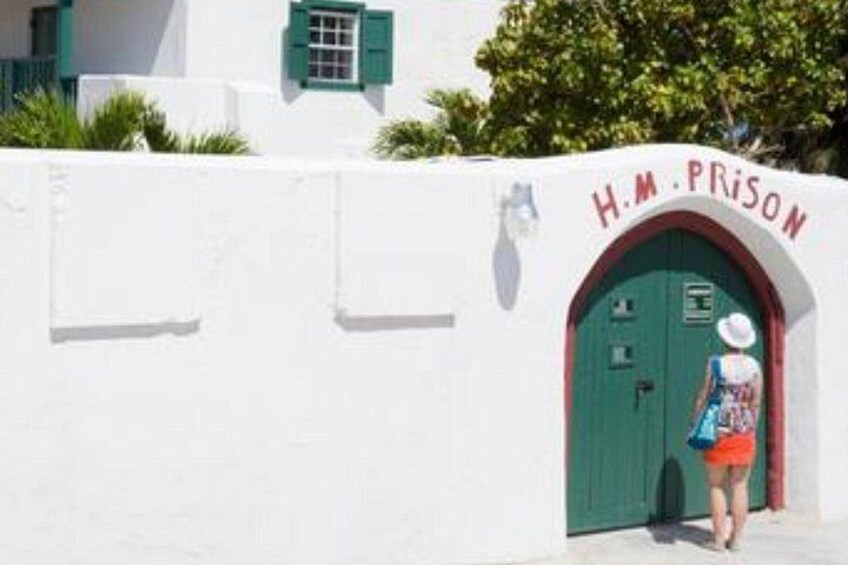 A white building with a green door labeled 'H.M. PRISON' and a person standing in front of it. 5