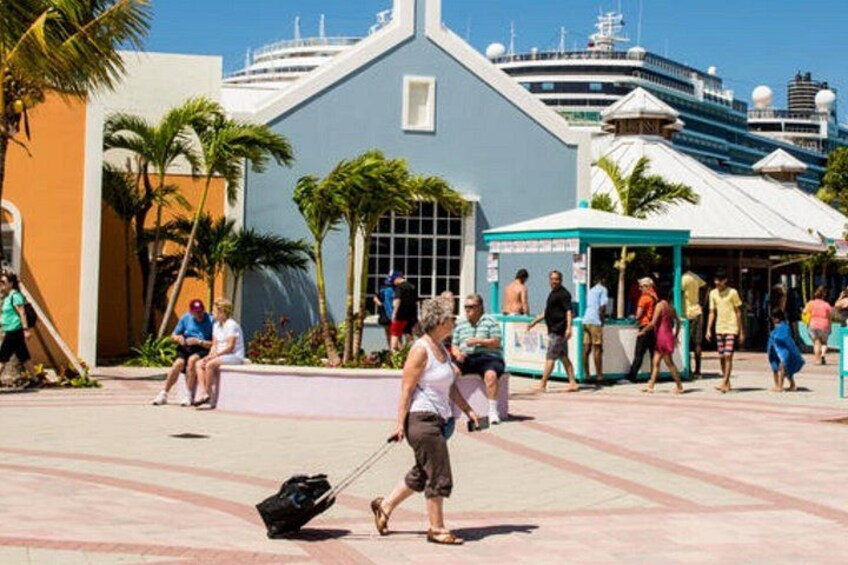 A bustling waterfront promenade with people walking, a large cruise ship docked in the background, and a distinctive building with a blue roof. 4