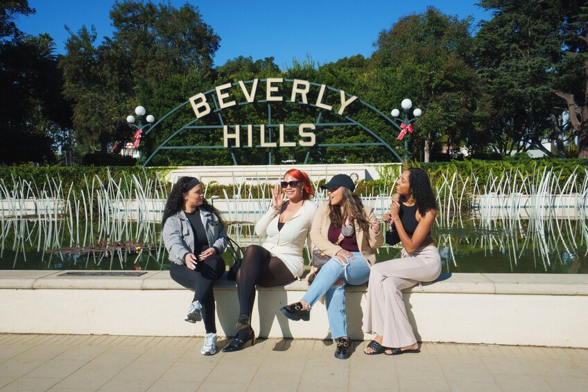 Vier Frauen sitzen auf einer Bank vor einem Schild mit der Aufschrift 'Beverly Hills'. 4
