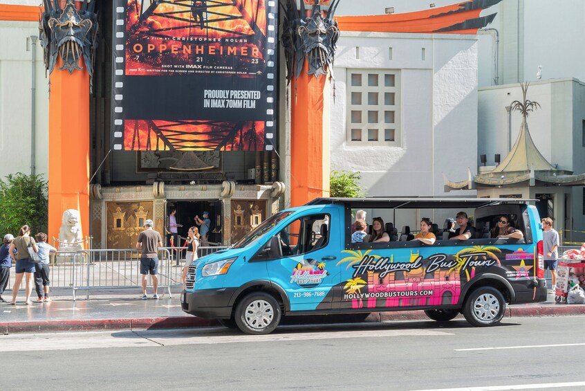 Ein blauer Reisebus mit Fahrgästen, vor einem Gebäude mit einem großen Filmplakat geparkt. 1