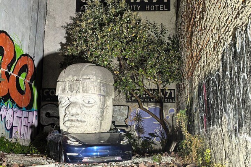 A stone head sculpture, a car, and graffiti on a wall with a sign for the City Hotel. 2
