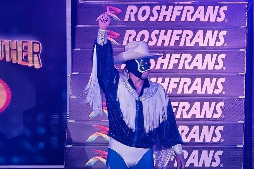 A person in a blue and white outfit with fringe details, standing in front of a backdrop with the text 'ROSHFRANS' repeated multiple times. 4