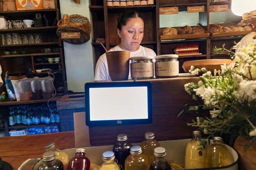 A bakery counter with jars of honey, a computer monitor, and shelves with baked goods. 2