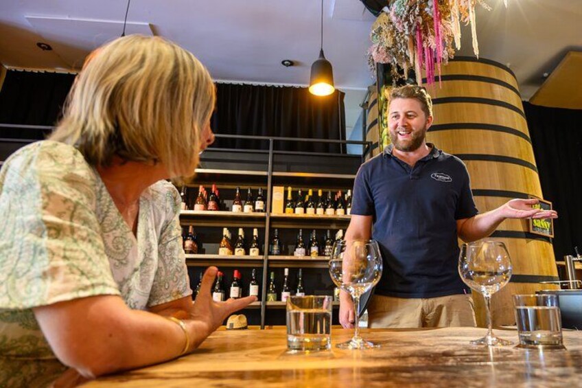 A person holding a wine glass, another person seated at a table with a bottle, and a wine rack in the background. 3