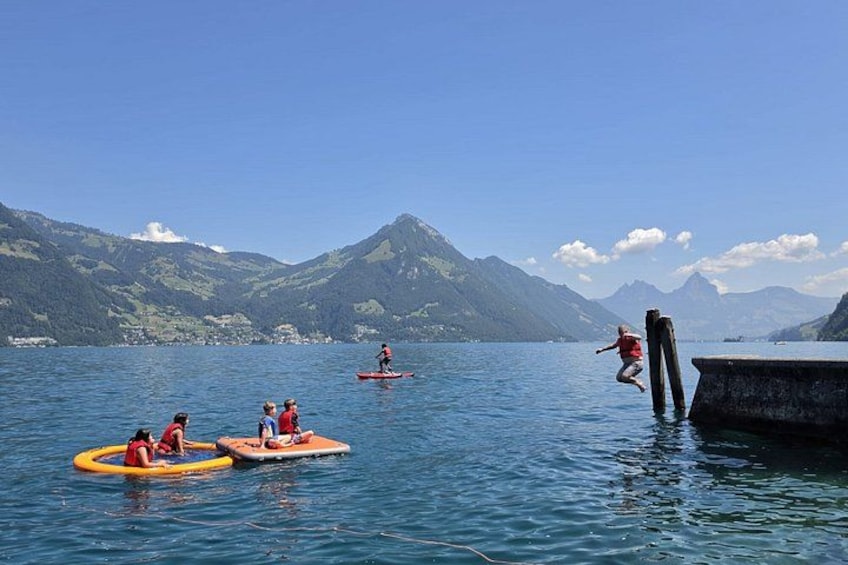 People on paddleboards and inflatable rings on a lake with mountains in the background. 1