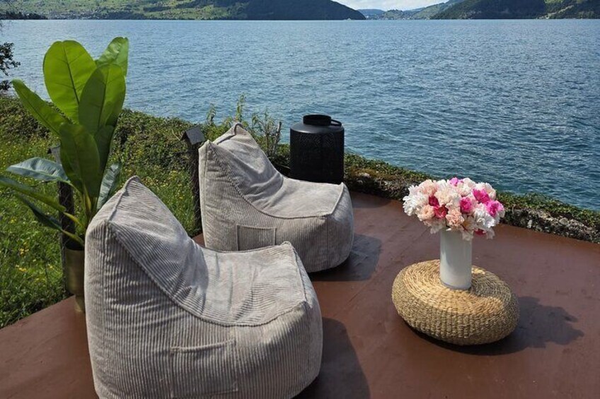 Outdoor seating with cushions and a woven stool by a lake. 4