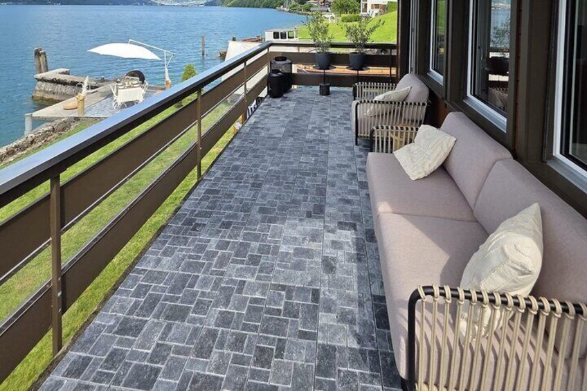 A balcony with a stone floor, a beige sofa, and a view of a lake. 2