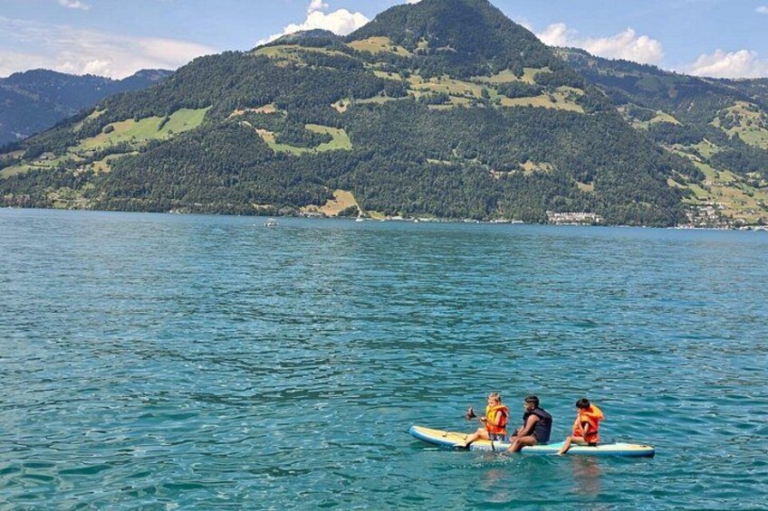 Three people on a paddleboard in a lake with mountains in the background. 3