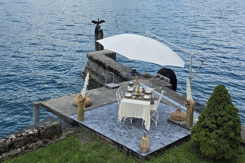 A dining setup by a lake with a table, chairs, and a white umbrella. 5
