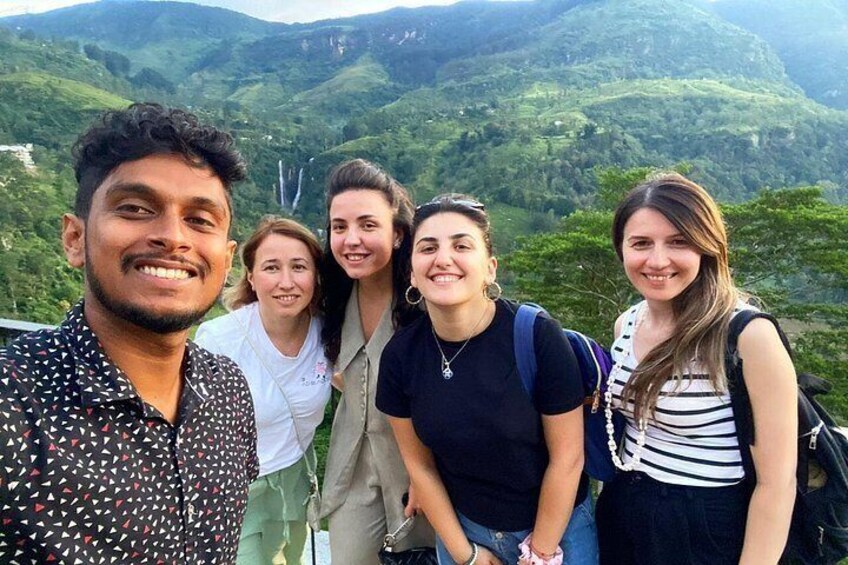 Un groupe de personnes se tient sur une montagne, avec une végétation luxuriante et une cascade en arrière-plan. 4