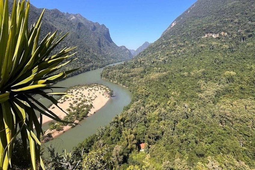Een rivier kronkelt door een bergachtig landschap met weelderige begroeiing en een klein dorp aan de rivieroever. 4