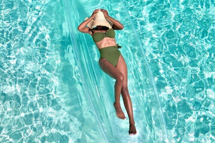 A person in a green swimsuit floating in a clear blue pool. 1
