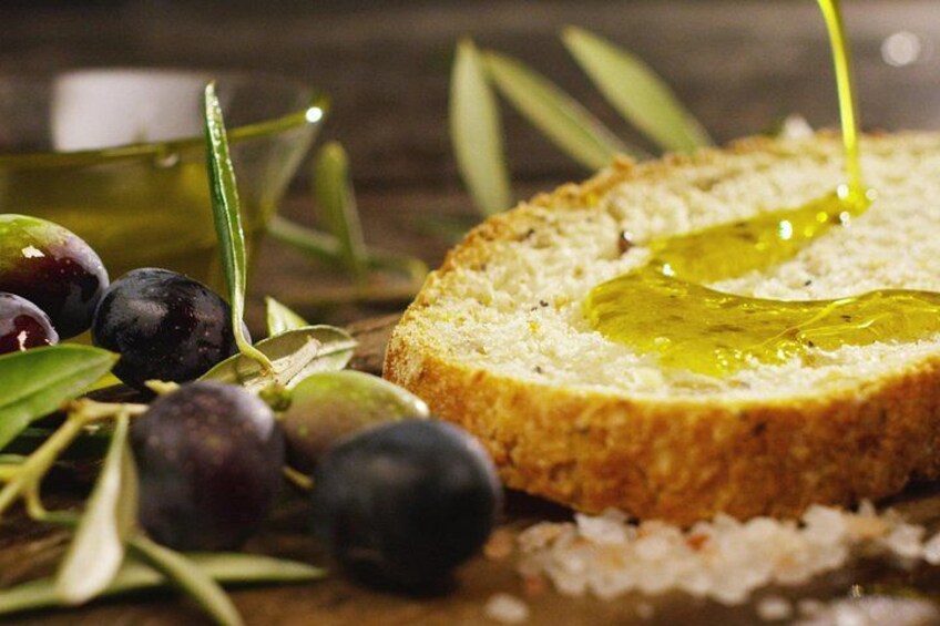 A slice of bread with olive oil, olives, and olive branches. 2