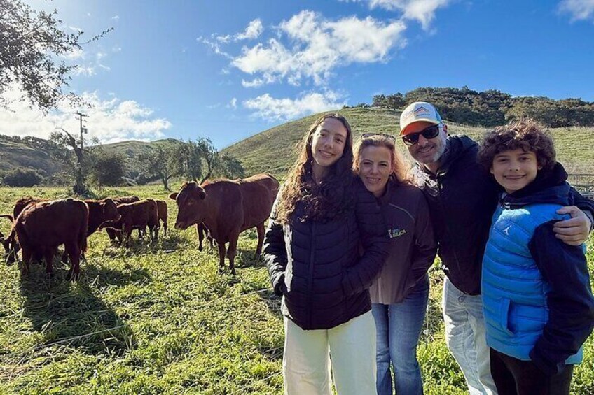 A family with cows in a grassy field with hills in the background. 1