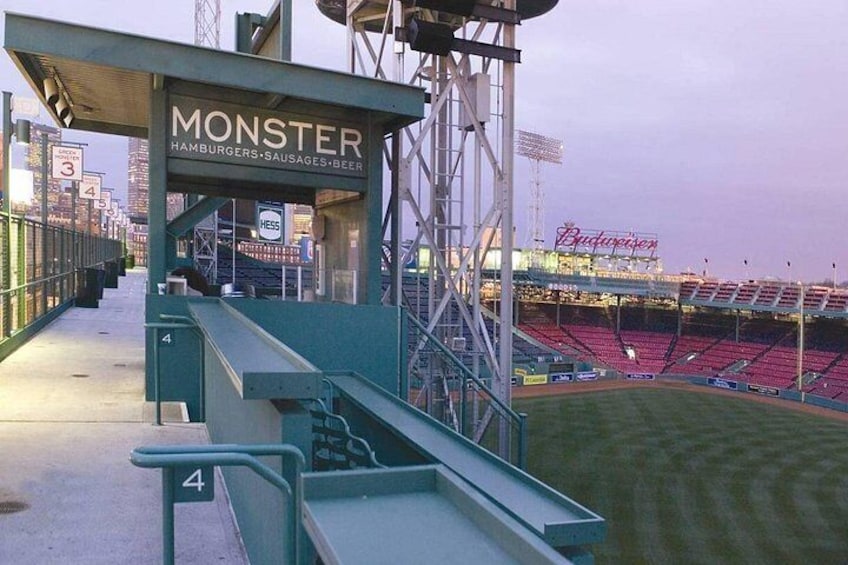 A baseball stadium with empty stands, a concession area labeled 'MONSTER' offering hamburgers, sausages, and beer, and a large 'Budweiser' sign in the background. 2