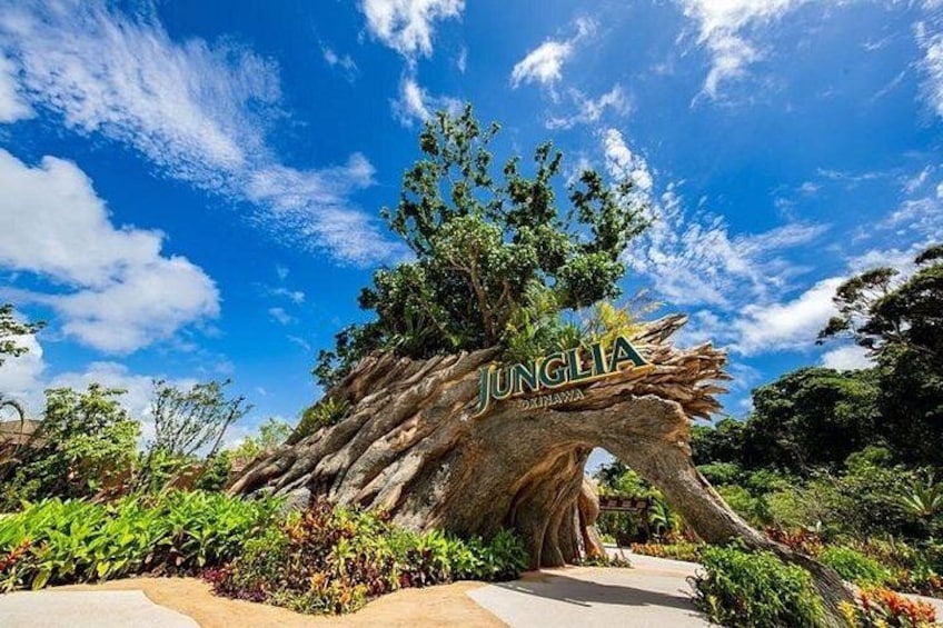 A large tree sculpture with the word 'JUNGIA' carved into it, surrounded by lush greenery and a clear blue sky. 1
