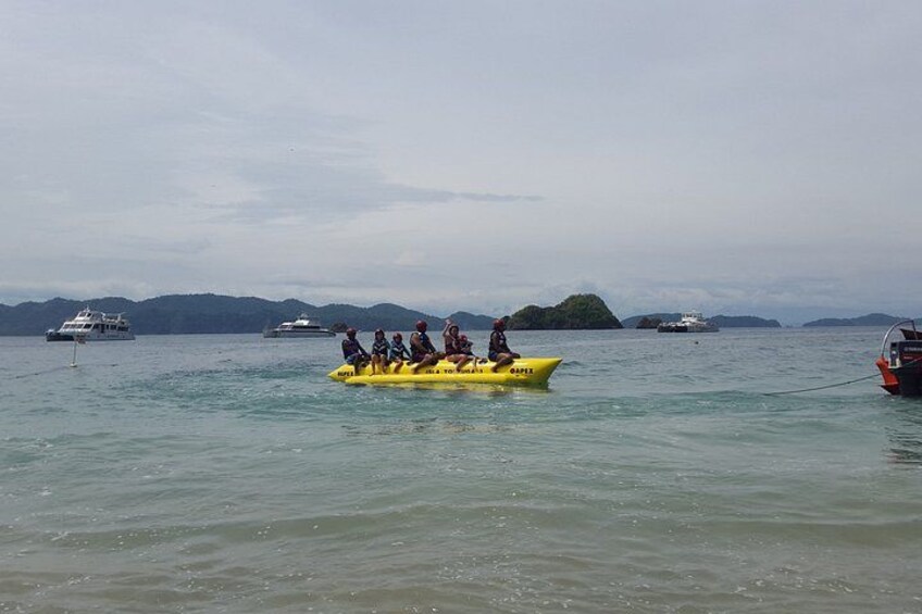 A yellow boat with people on a calm sea, surrounded by larger boats and distant islands. 4