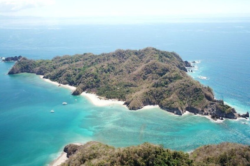 A tropical island with clear turquoise waters, a sandy beach, and dense green vegetation. 1