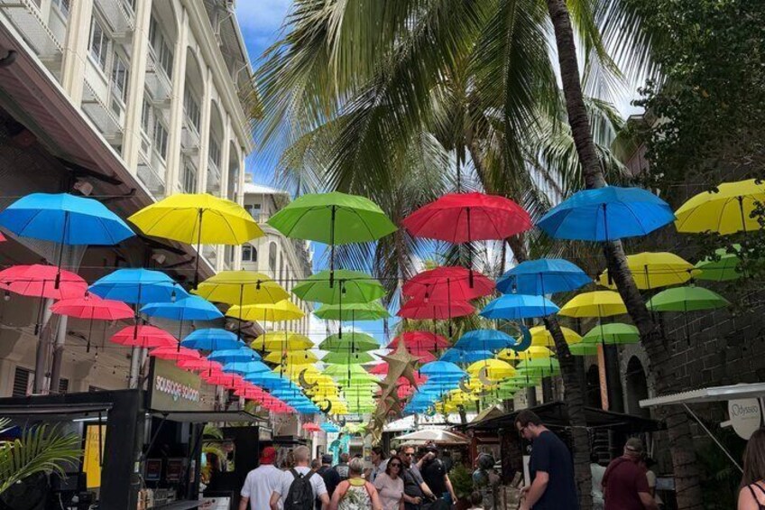 A street with colorful umbrellas hanging overhead, palm trees, and buildings. 2