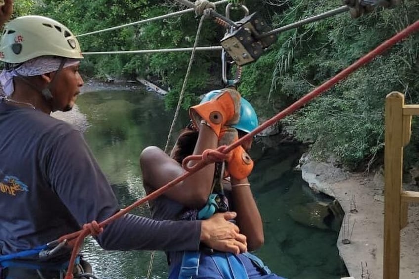 A person rappelling down a rope with a harness and helmet, surrounded by greenery and a river. 5