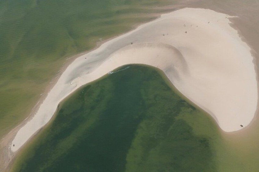 A coastal landscape with a large sandbar, green water, and a small island. 5