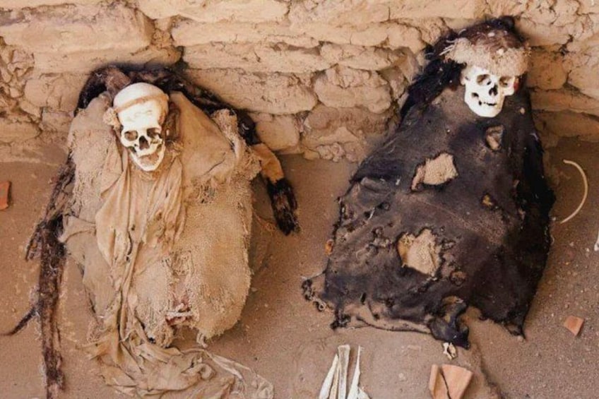 Deux corps momifiés, dont les restes squelettiques sont enveloppés de tissu, reposent sur le sol à l’intérieur d’une structure en pierre. 5