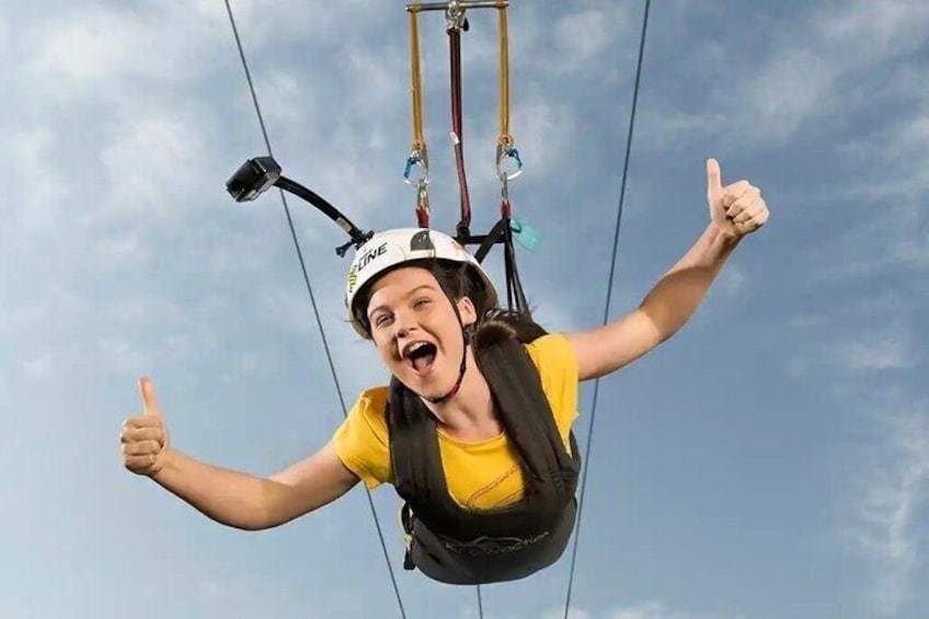 A person in a yellow shirt and helmet, suspended by a harness, giving a thumbs-up. 2