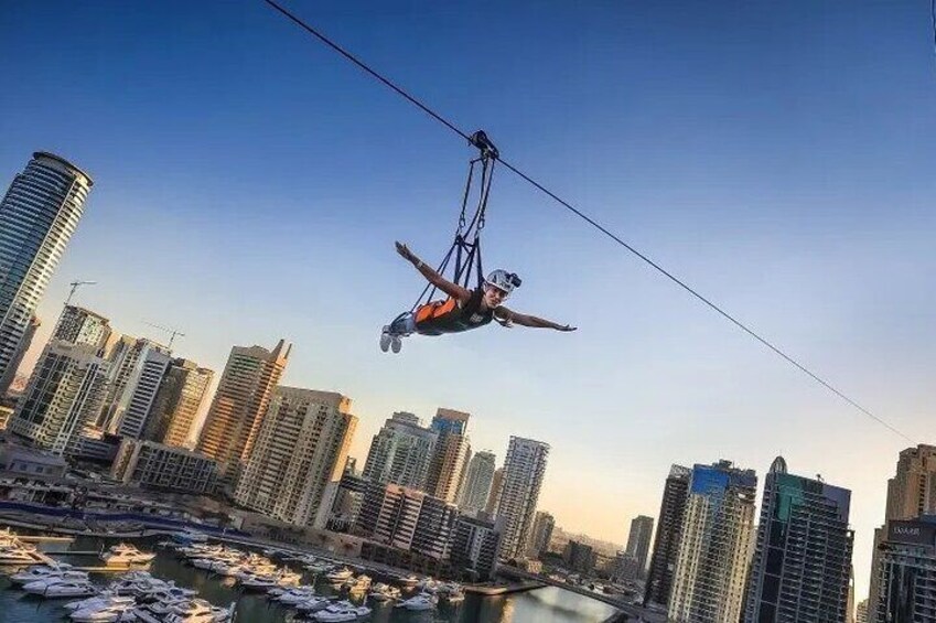 A person suspended by a cable in an urban setting with high-rise buildings and a marina. 4